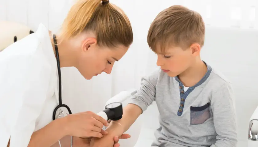 Lekarka bada rękę chłopca dermatoskopem, sprawdzając znamię dysplastyczne.