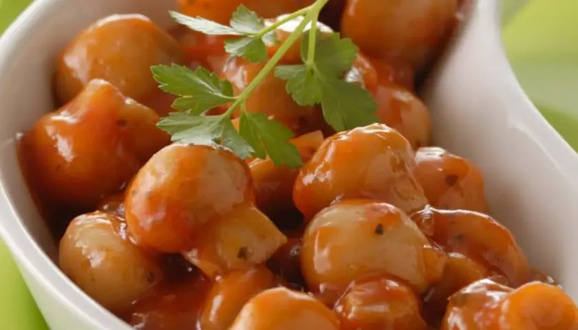 Champignons à la grecque, petits et tendres, nappés d'une sauce savoureuse et garni d'une feuille de persil.