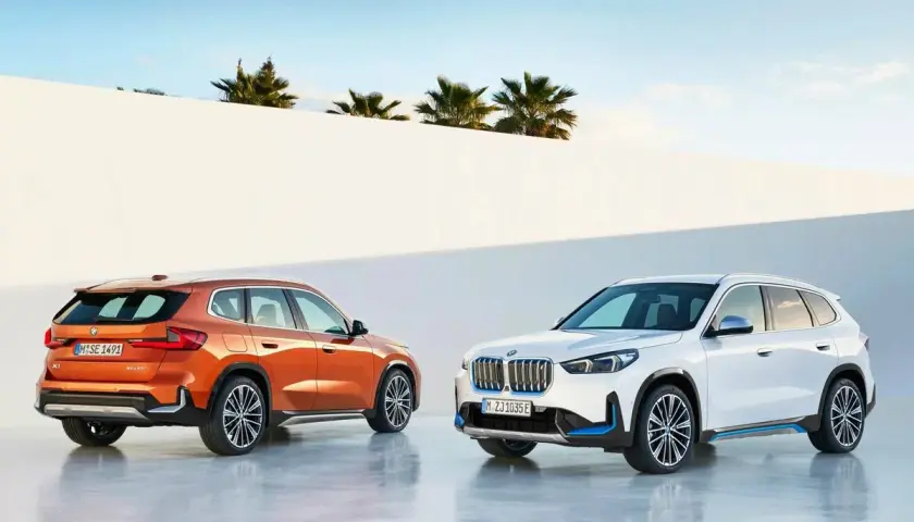 Dos BMW Serie X, uno naranja y otro blanco, posan ante un muro blanco y palmeras.