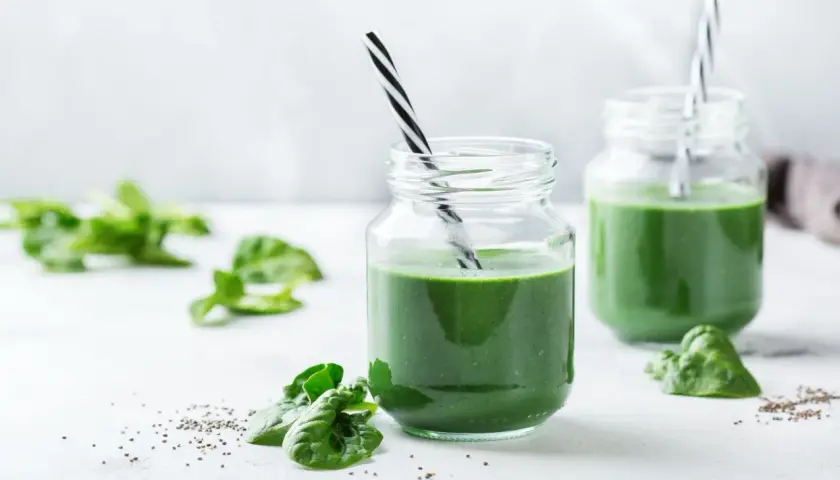 Två glas med grön smoothie, garnerade med spenatblad och chiafrön. Tänk på eventuella spirulina biverkningar innan du dricker.