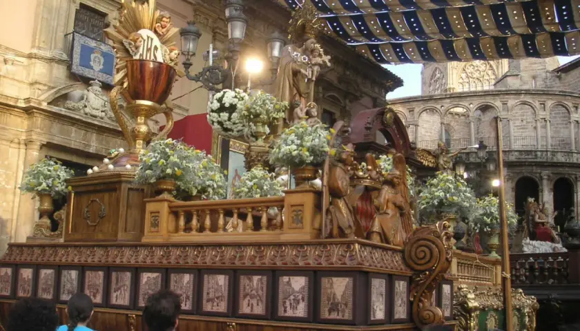 Procesión religiosa con un elaborado trono de madera adornado con flores y figuras. El **corpus 2026** se prepara para la festividad.