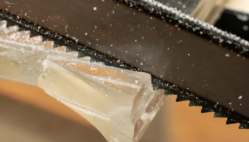 Sågtänder skär genom ett tjockt, genomskinligt material. Små bitar av kapa plexiglas flyger runt.