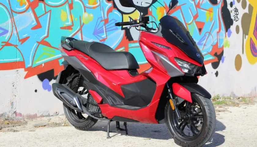 Scooter SYM Jet X 125 rojo brillante, con diseño deportivo, frente a un muro con grafitis coloridos. ¡Un estilo que inspira buenas opiniones!