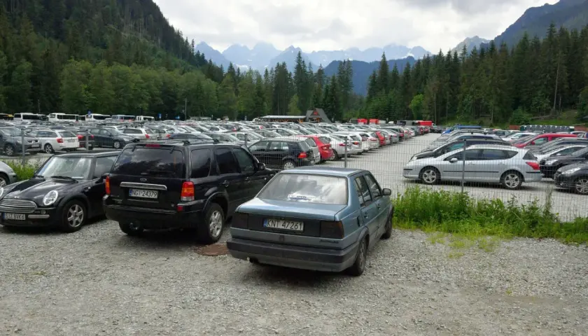 Duży parking samochodowy u podnóża gór, z widokiem na Tatry, jakby eic morskie oko patrzyło z góry.