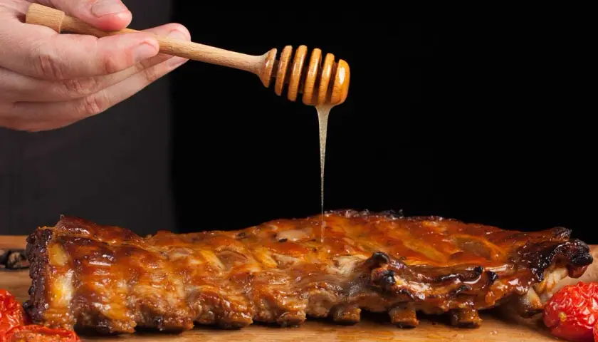 Costillas a la miel jugosas, bañadas con miel dorada de un palillo de madera. Acompañadas de tomates asados.