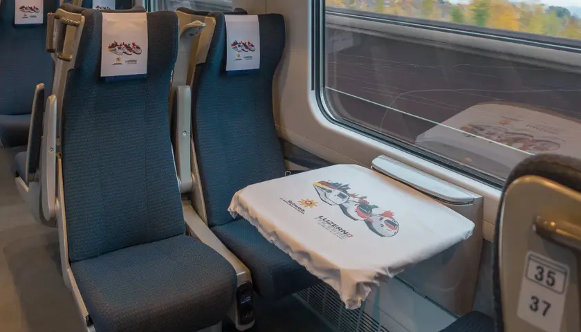 Sitze in einem ece train mit Kopfstützen und einem Tisch, der mit einem Tuch mit Zugmotiven bedeckt ist.