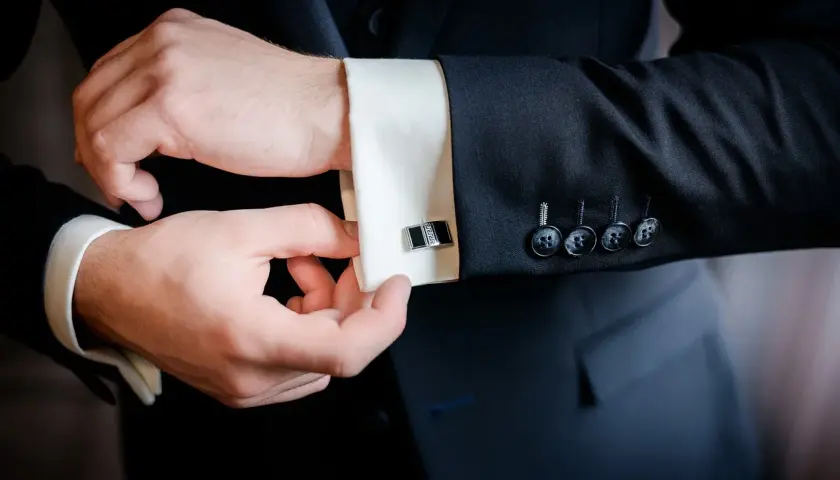Mężczyzna zapina mankiety koszuli, przygotowując się do ważnego wydarzenia. Eleganckie spinki dodają stylu.