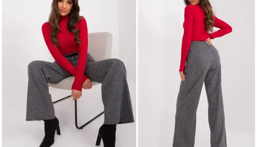 Modelka w czerwonym golfie i szarych, szerokich spodniach z wysokim stanem, które delikatnie zwężają się ku dołowi (tapered).