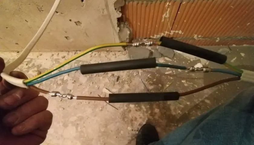 Ręczne skręcanie kabli elektrycznych, przygotowanie do izolacji. Widać połączenia przewodów w trakcie pracy.