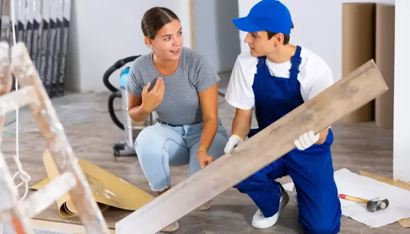 Un artisan montre une lame de parquet à une cliente. Elle s'interroge sur quels travaux peut on déduire des impôts pour ce type de rénovation.