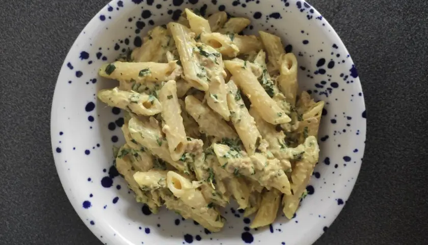 Penne z kremowym sosem, kawałkami tuńczyka i zieloną natką pietruszki, podane w talerzu w granatowe cętki.