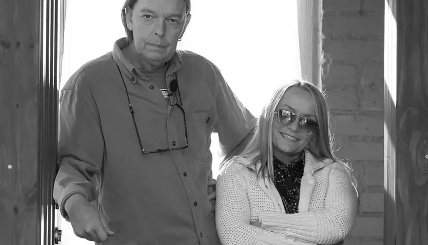 Małgorzata Ostrowska z mężem, uśmiechnięta kobieta w okularach przeciwsłonecznych i mężczyzna z długimi włosami, stoją obok siebie.