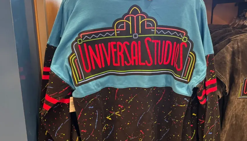 Turkusowy longsleeve z neonowym napisem "Universal Studios" i kolorowymi plamkami na czarnym tle. Idealny na wycieczkę do parku rozrywki!