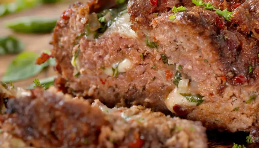 Un succulento polpettone ripieno, con formaggio filante e erbe aromatiche, pronto per essere gustato.