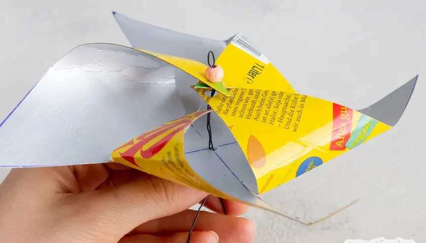 Bastelanleitung für ein Windrad: Eine Hand hält ein selbstgemachtes Windrad aus einer Getränkeverpackung, das sich dreht. Eine Vorlage zum Windrad basteln ist hier zu sehen.