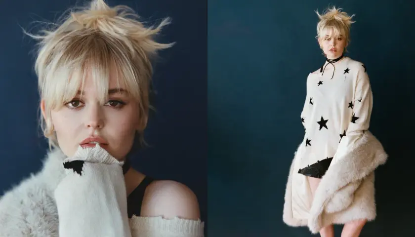 Emily Alyn Lind med rufsigt blont hår, bär en stickad tröja med stjärnor och en pälskappa.
