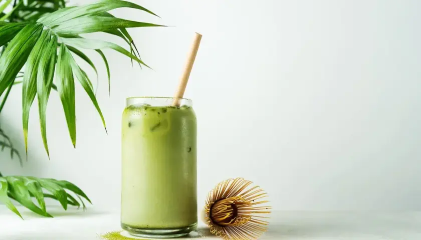 Orzeźwiające matcha latte z lodem i bambusową słomką, obok bambusowa miotełka. Poznaj niezwykłe matcha właściwości!