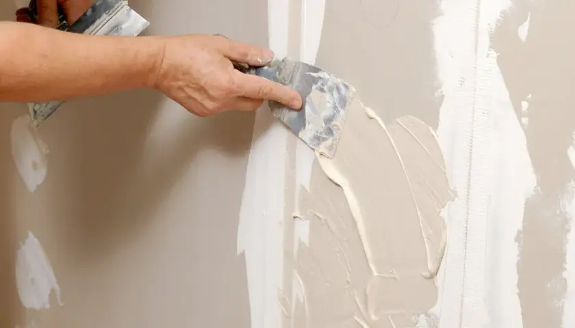 Mano stende stucco su una giuntura di cartongesso, ricordando che il cartongesso ha un verso.
