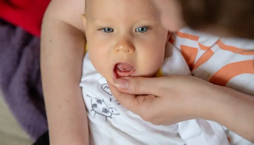 Niemowlę z niebieskimi oczami, u którego widoczne są rozpulchnione dziąsła, sugerujące ząbkowanie.