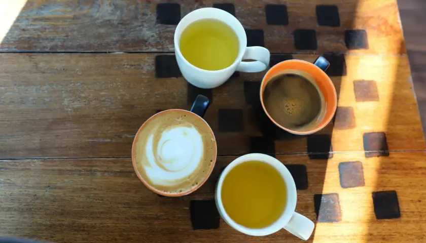 Kawa i herbata na drewnianym stole. Czy zielona herbata pobudza? Obok niej kawa latte i espresso.