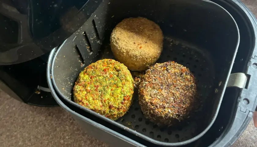 Trzy okrągłe kotleciki z sera typu włoskiego, obtoczone w ziołach i przyprawach, gotowe do smażenia w frytkownicy beztłuszczowej.