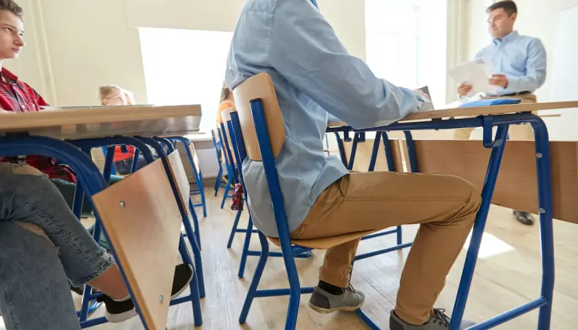 Uczniowie siedzą w ławkach, słuchając nauczyciela. Pomoc nauczyciela w szkole podstawowej to wsparcie w nauce i organizacji.