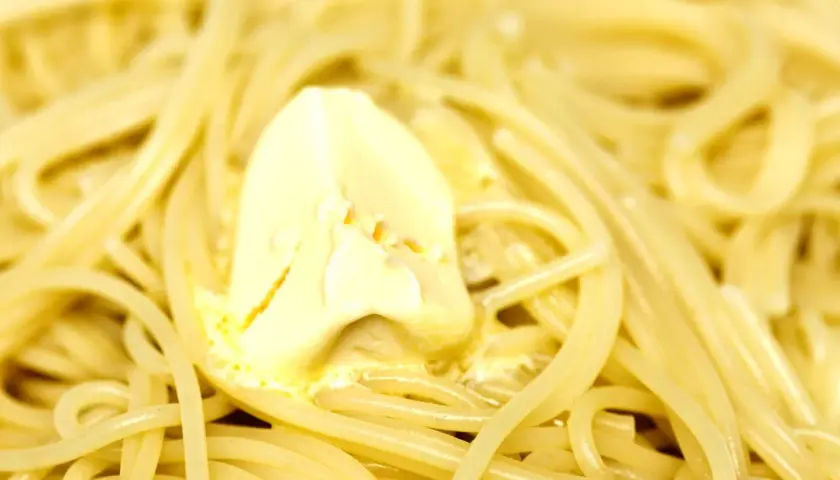 Un piatto di pasta in bianco, con spaghetti conditi da una generosa porzione di burro che si scioglie.
