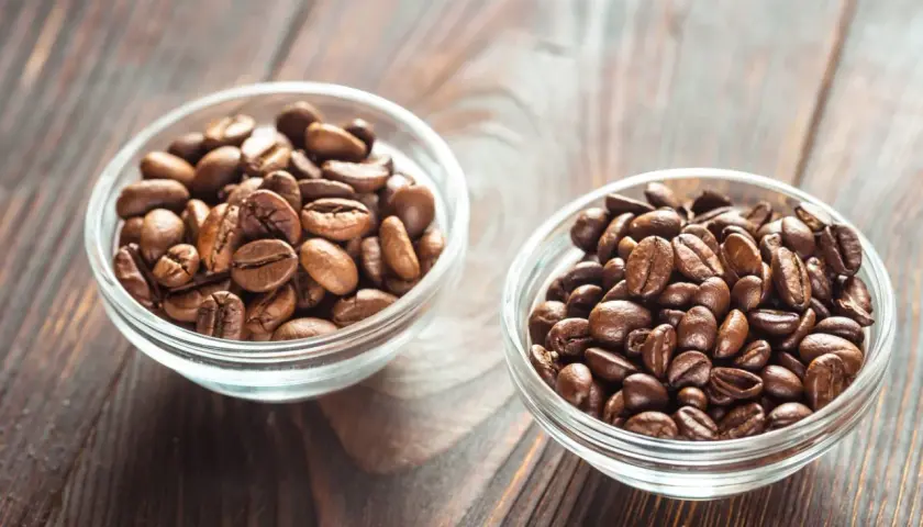 Dwie miseczki z ziarnami kawy: jedna z jaśniejszymi ziarnami arabiki, druga z ciemniejszymi, tworzącymi idealną mieszankę arabica i robusta.