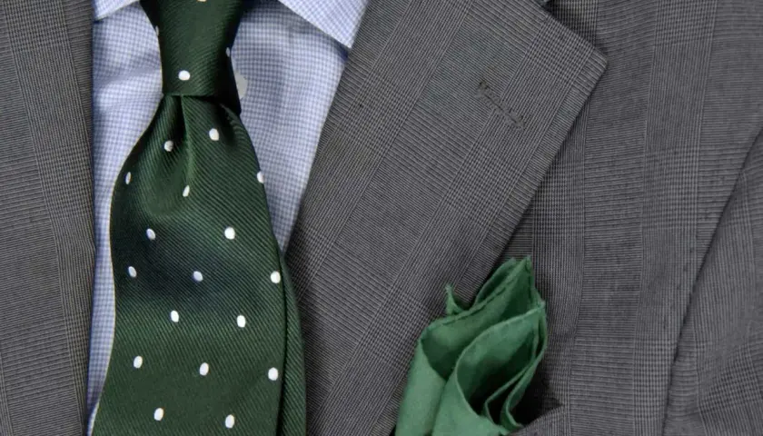 Elegancki zestaw: niebieska koszula, zielony krawat w kropki i szara marynarka w kratę. Idealna odpowiedź na pytanie: jaki krawat do niebieskiej koszuli.