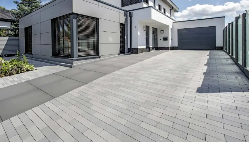 Moderne Einfahrt pflastern mit grauen Steinen. Das Haus hat eine graue Fassade und weiße Akzente.