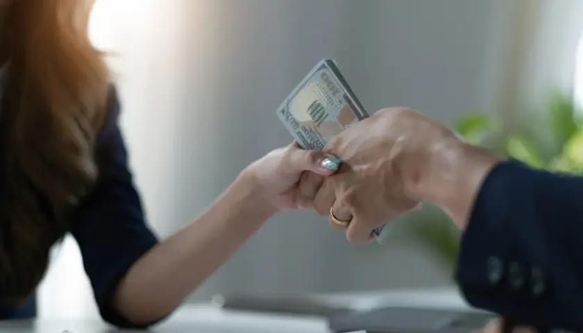 Dwie ręce przekazują sobie plik banknotów. To symboliczny moment zawarcia umowy pożyczki.