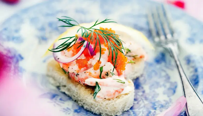 En läcker toast Skagen med räkor, rom, dill och rödlök på en blåvit tallrik.