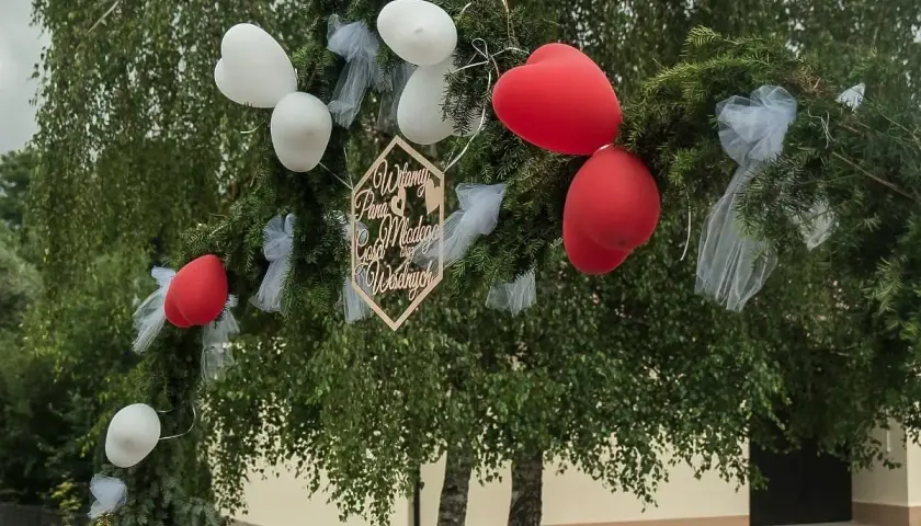 Drewniany napis "Witamy Parę Młodą" na gałęziach, ozdobionej balonami i tiulem. Piękne brama weselna pomysły.