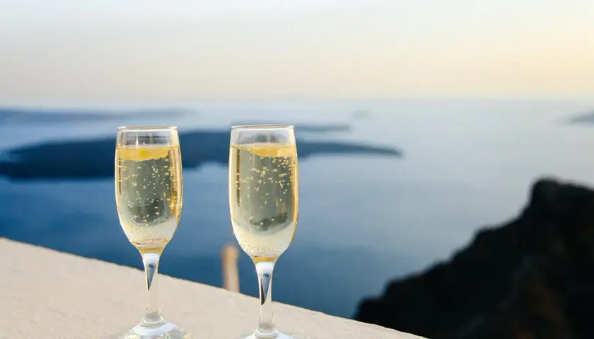 Zwei Gläser Champagner mit Bläschen vor einer Meereslandschaft. Die Frage, wie lange ist Champagner haltbar, beschäftigt Genießer.