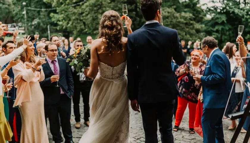 Para młoda wznosi toast, a goście, wśród których widać rodziców, świętują.