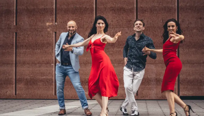 Dwie pary tańczą gorący zouk. Kobiety w czerwonych sukienkach, mężczyźni w eleganckich strojach.