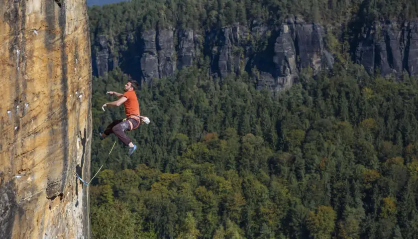 Ein Mann klettert an einer Felswand in Tschechien. Im Hintergrund erstreckt sich ein dichter, grüner Wald.