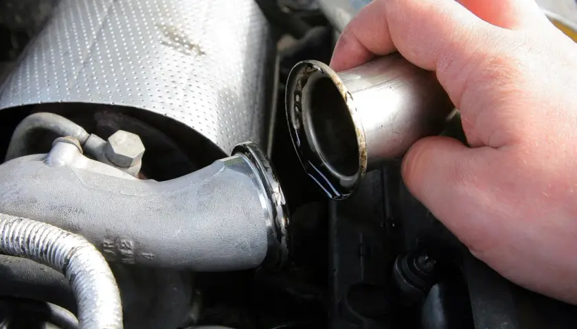 Dłoń trzymająca metalową rurkę z widocznymi śladami oleju, część układu dolotowego turbiny auto.