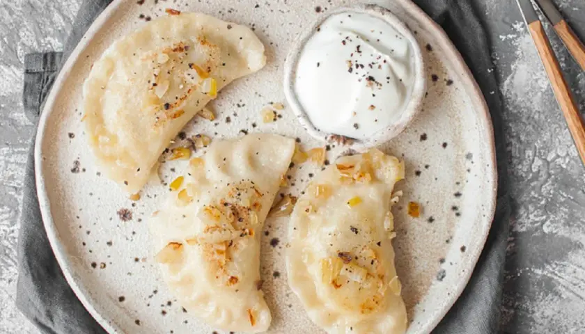 Jak odgrzać pierogi w mikrofali? Na talerzu ułożone pierogi z cebulką i śmietaną, gotowe do szybkiego podgrzania.