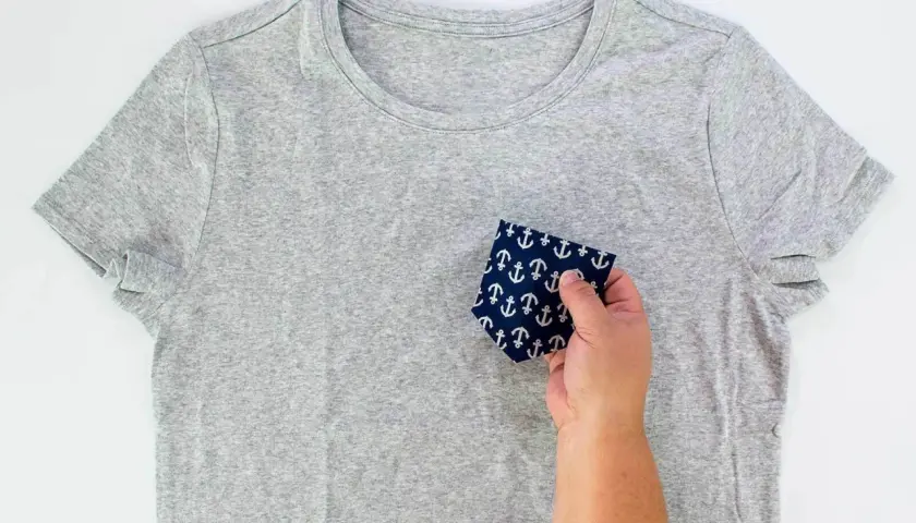 A hand holds a navy fabric with white anchors, demonstrating how to sew front pockets on pants.