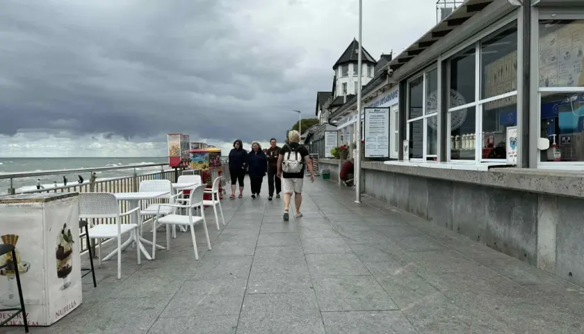 Spacer w Sarbinowie, gdy pada. Ludzie idą promenadą obok barów z lodami i kawiarni, szukając atrakcji.