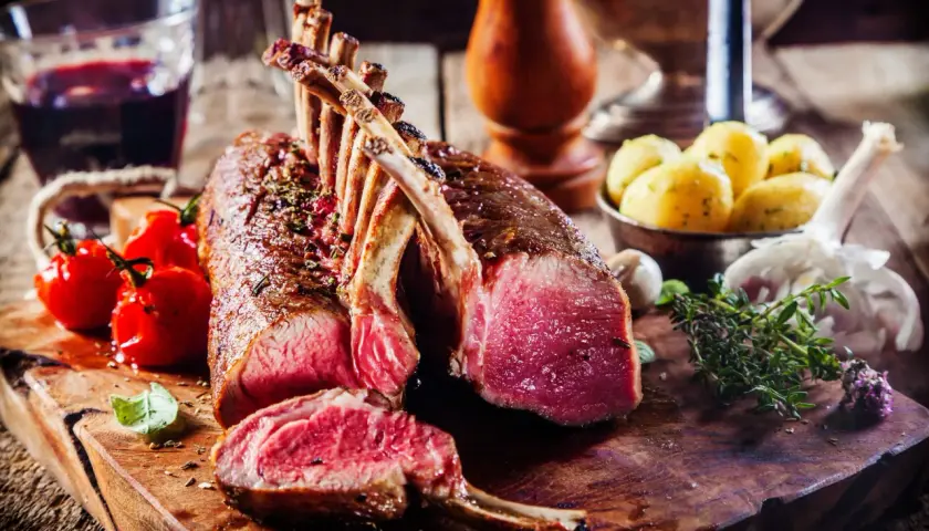 Un succulent carré d'agneau rôti, accompagné de tomates cerises, de pommes de terre et d'une touche d'herbes fraîches.