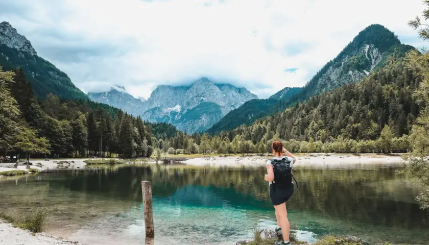 Frau mit Rucksack genießt den Blick auf einen türkisfarbenen See und die Berge. Perfekter Ort zum Wandern in Slowenien.