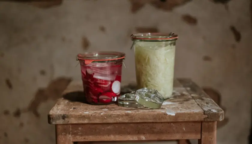 Zwei Gläser mit fermentierten Lebensmitteln: links eingelegte Radieschen, rechts fermentiertes Sauerkraut.
