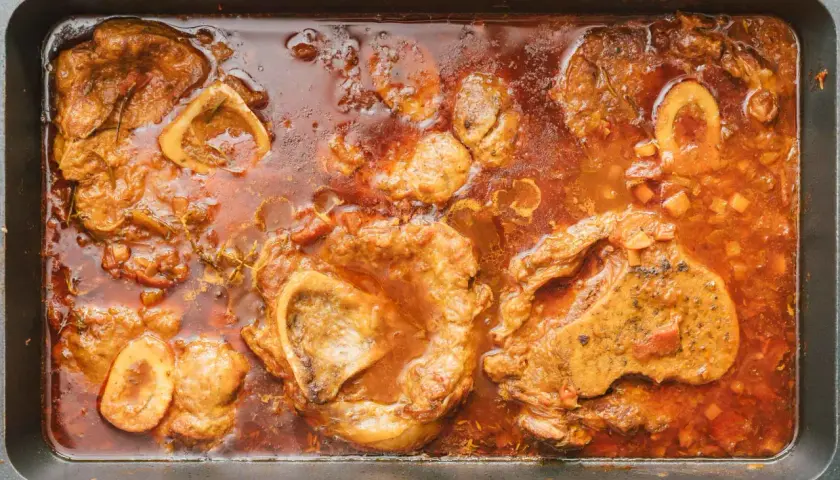 Herzhaftes Ossobuco-Rezept original italienisch: Kalbshaxenscheiben schmoren in aromatischer Sauce mit Gemüse und Kräutern in einer Bratpfanne.