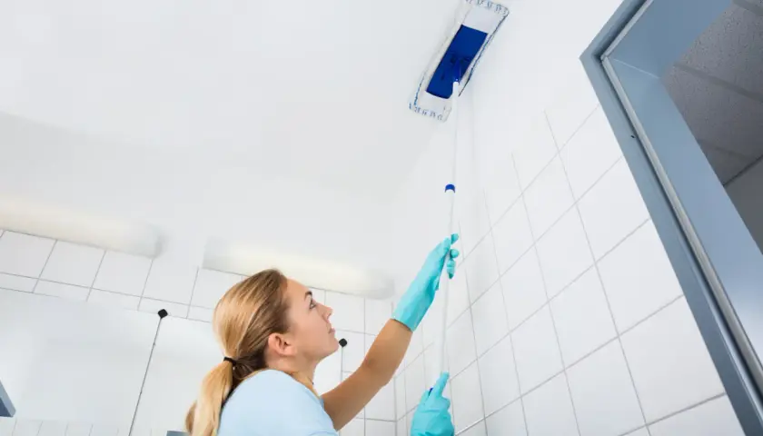 Femme nettoyant le plafond avec une raclette. Le sens de pose du lambris PVC au plafond est important pour un résultat impeccable.