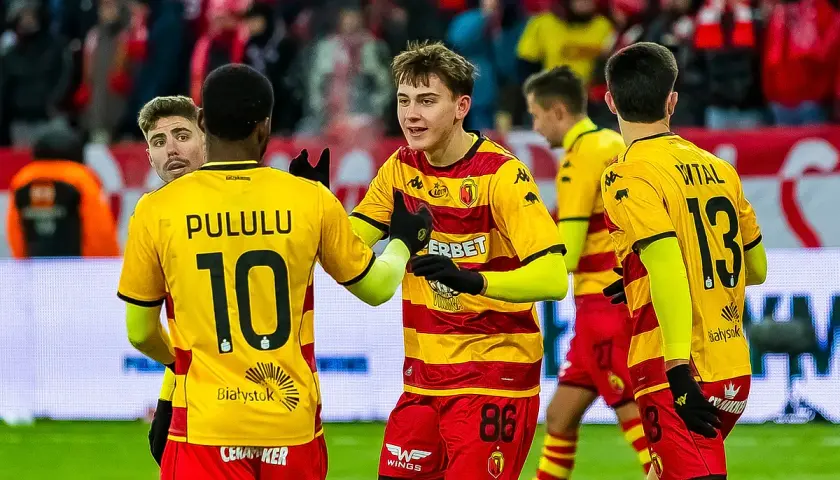 Piłkarze Jagiellonii Białystok świętują. Na boisku w meczu przeciwko Górnikowi Zabrze, zawodnicy w żółto-czerwonych strojach cieszą się z sukcesu.
