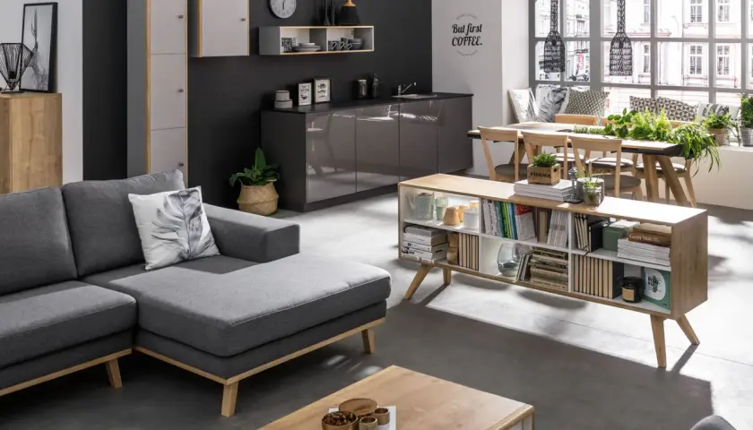 Nowoczesny salon z szarą kanapą i ciemną ścianą. Kolor ścian w salonie podkreśla jasne meble i dodatki.