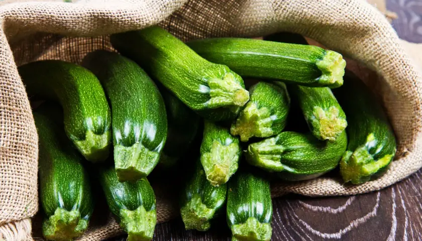 Frische, grüne Zucchini quellen aus einem Jutesack. Diese gesunde Gemüsesorte ist perfekt für leichte und nahrhafte Gerichte.