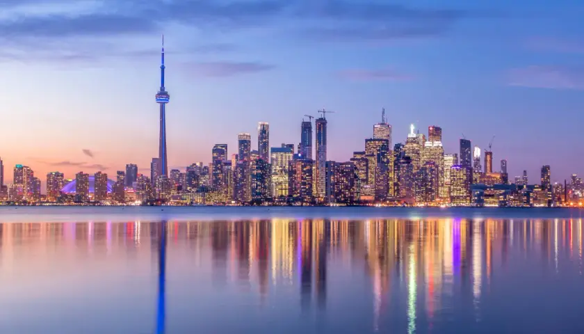 Toronto Skyline bei Dämmerung, ein Muss für jeden Besucher. Der CN Tower ragt empor, beleuchtete Wolkenkratzer spiegeln sich im Wasser.